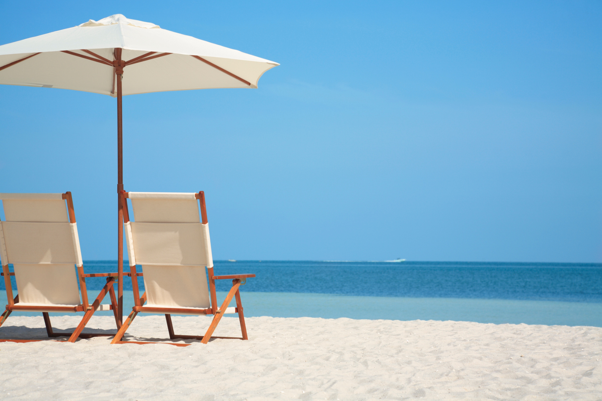 An upscale white beach umbrella and wooden lounge chairs facing a turquoise ocean